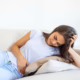 woman painful expression holding hands against belly suffering menstrual period painsitting sad home bed having tummy cramp female health concept 1200x675